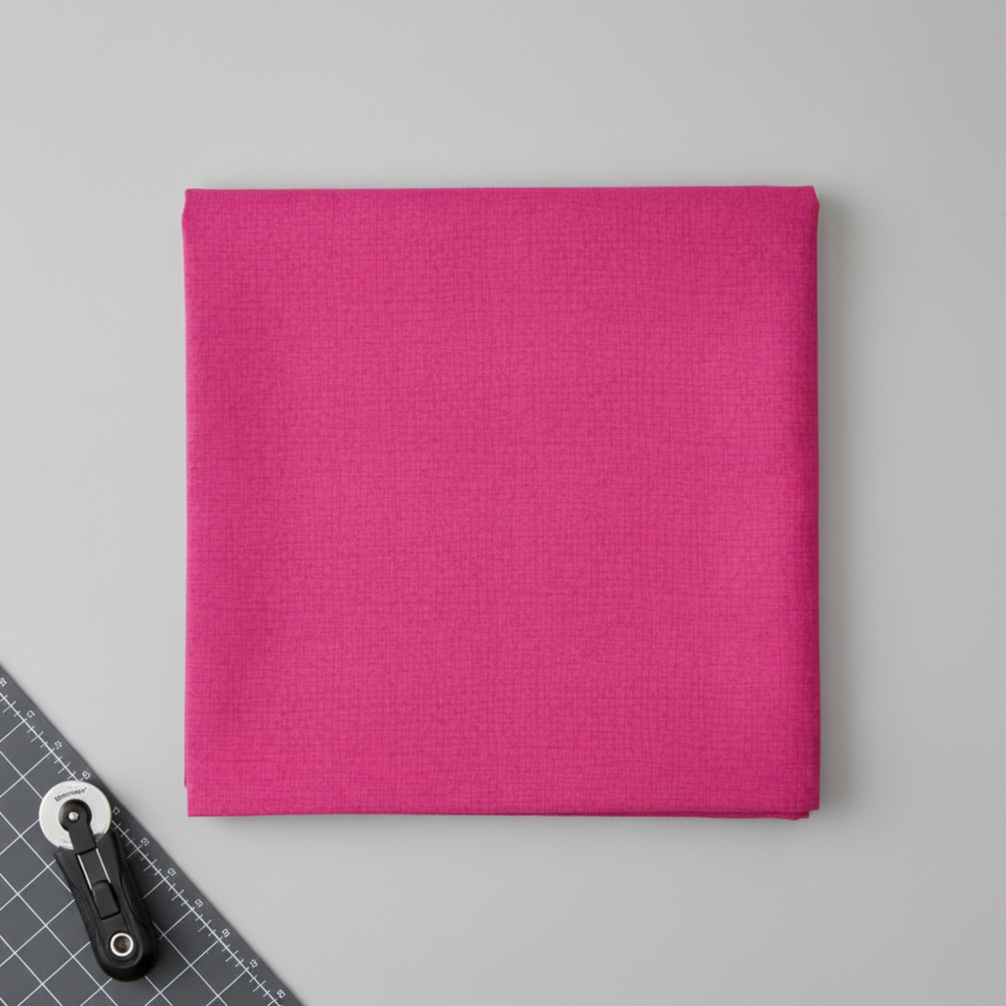 Thatched Fuchsia fabric by Robin Pickens for Moda Fabrics partially folded on a cutting mat with a rotary cutter in a clean quilting workspace. 