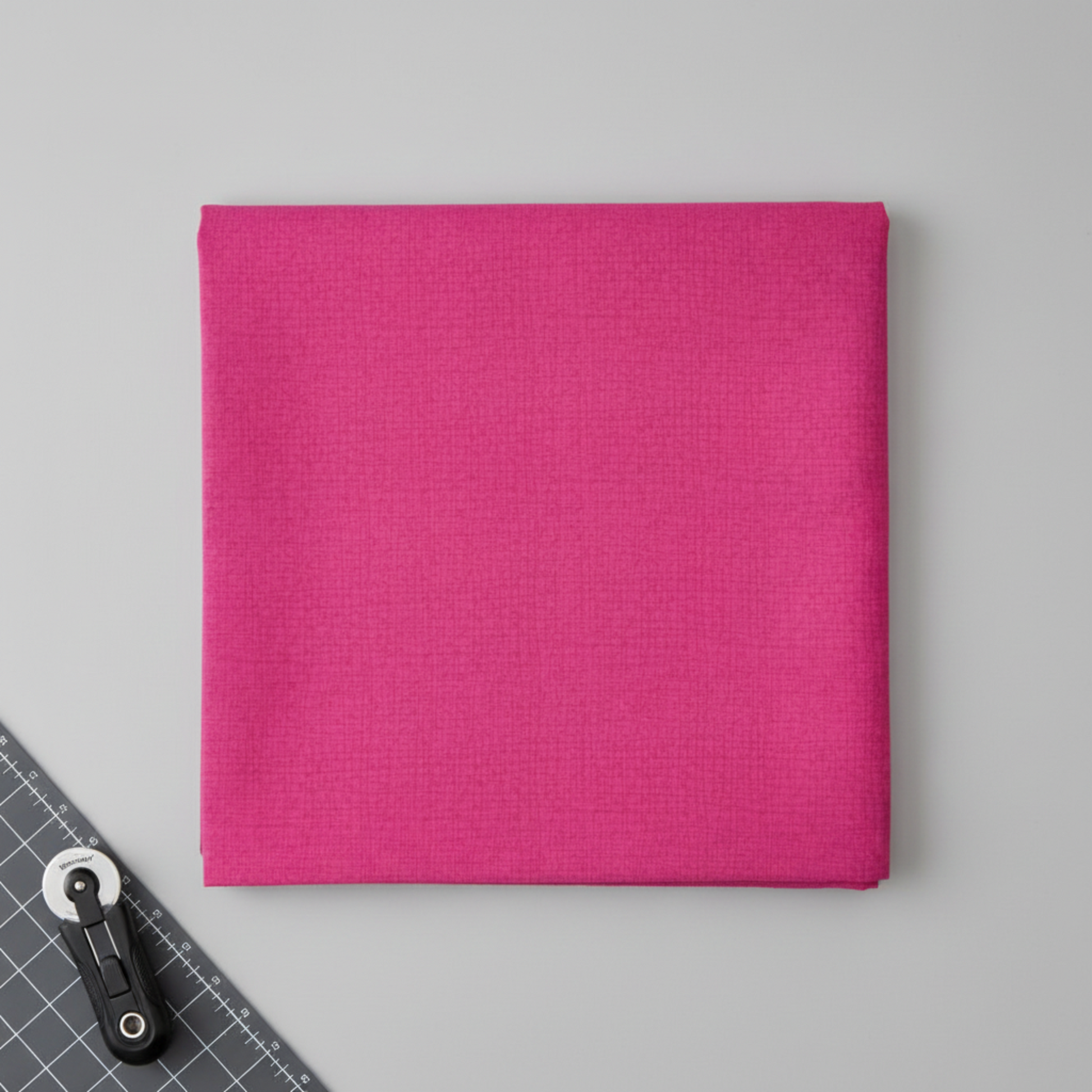 Thatched Fuchsia fabric by Robin Pickens for Moda Fabrics partially folded on a cutting mat with a rotary cutter in a clean quilting workspace. 