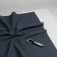 Thatched Soft Black quilting cotton by Robin Pickens for Moda Fabrics — partially folded fabric on a light grey surface with a cutting mat corner and rotary cutter. Deep navy-black ground with signature crosshatch texture. Coordinating fabrics and quilt patterns available at IraRobi Quilts.