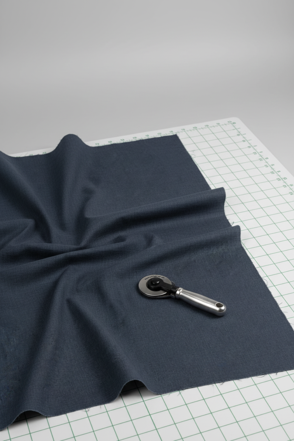 Thatched Soft Black quilting cotton by Robin Pickens for Moda Fabrics — partially folded fabric on a light grey surface with a cutting mat corner and rotary cutter. Deep navy-black ground with signature crosshatch texture. Coordinating fabrics and quilt patterns available at IraRobi Quilts.
