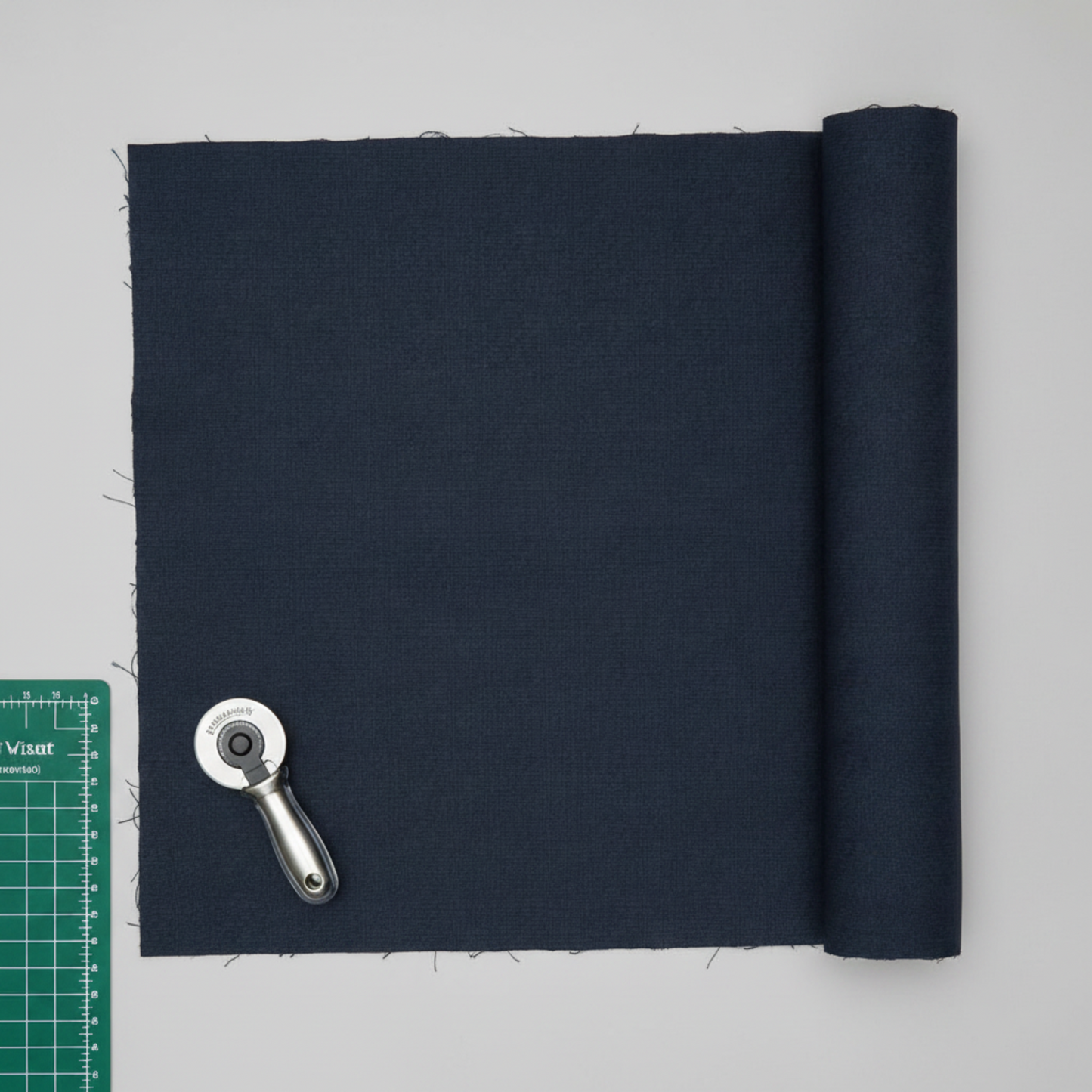 Thatched Soft Black quilting cotton by Robin Pickens for Moda Fabrics — partially folded fabric on a light grey surface with a cutting mat corner and rotary cutter. Deep navy-black ground with signature crosshatch texture. Coordinating fabrics and quilt patterns available at IraRobi Quilts.