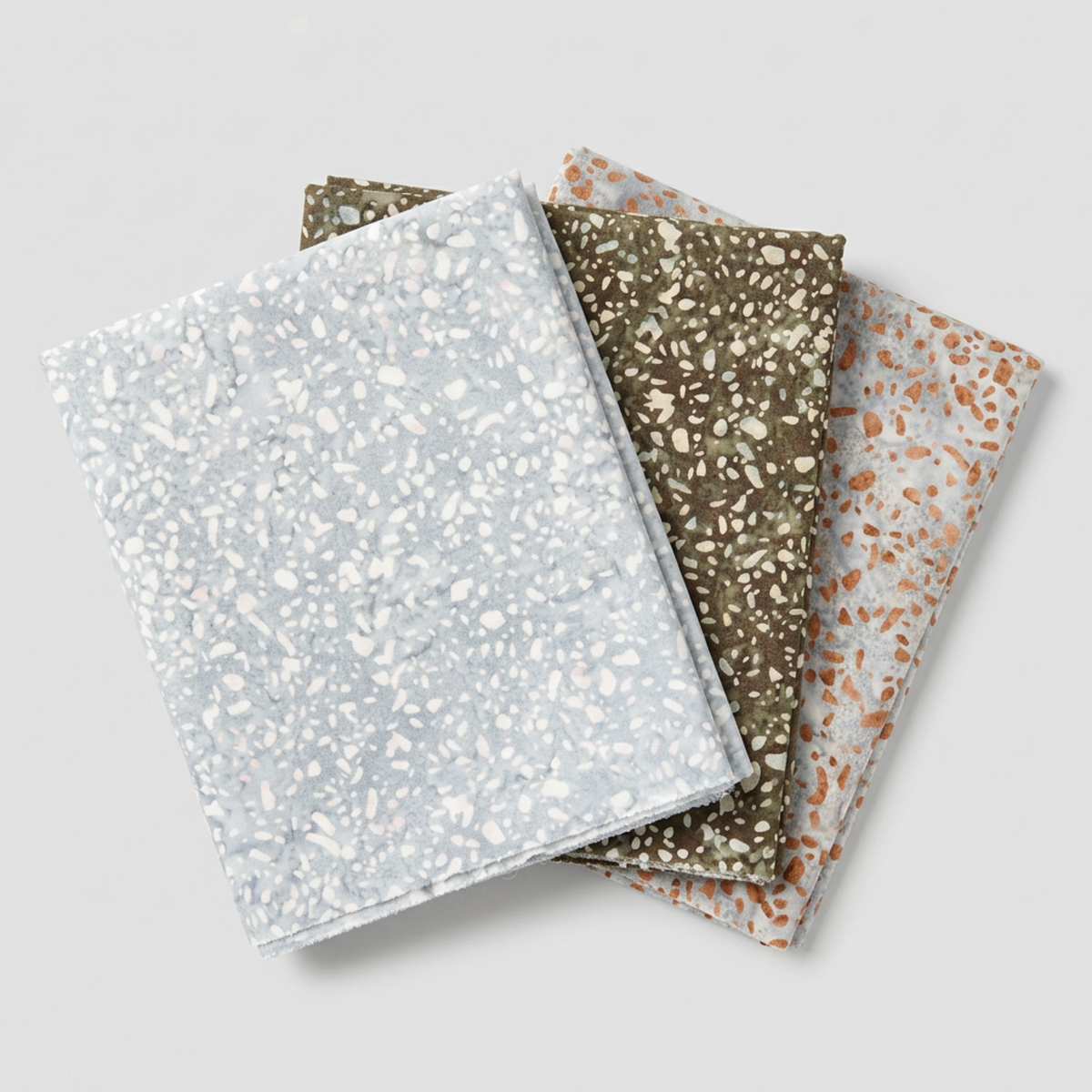 Terrazzo Powdered Pearl Fabric by Riley Blake Designs at the front of a three-fabric fan, with coordinating khaki and peach-flecked gray fabrics.