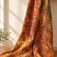Windsong Tonga Batiks Floral Medallions Sienna fabric draped from a wooden shelf in natural light, showing layered rust, ochre, plum, coral, and olive botanical motifs.