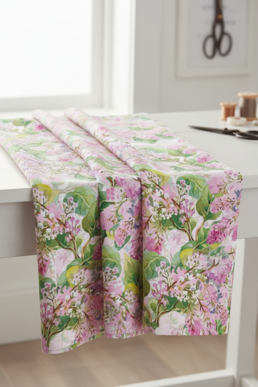 Decoupage Pink Lilac floral quilting fabric draped over a white sewing table, showing its pink, lilac, and green botanical print.