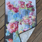 Vase with Flowers wall quilt on wooden decking, with the lower-right corner folded back to show pale-grey patterned backing, dark binding, and diagonal quilting.