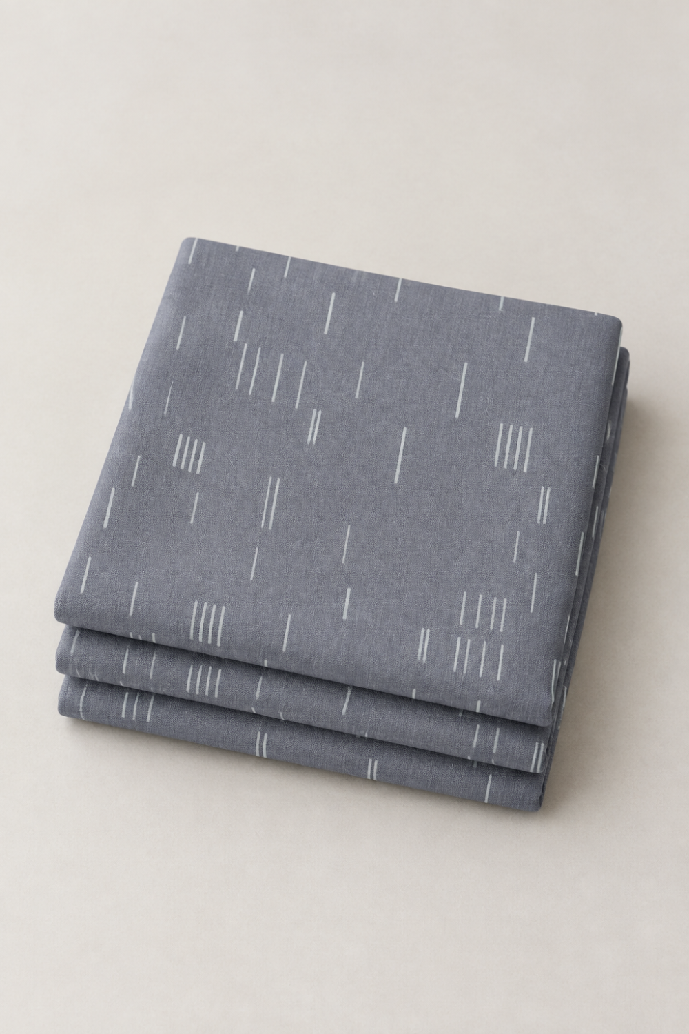 Folded stack of Celestial Strokes Aluminum fabric by Zen Chic for Moda Fabrics, featuring fine white marks on aluminum gray.
