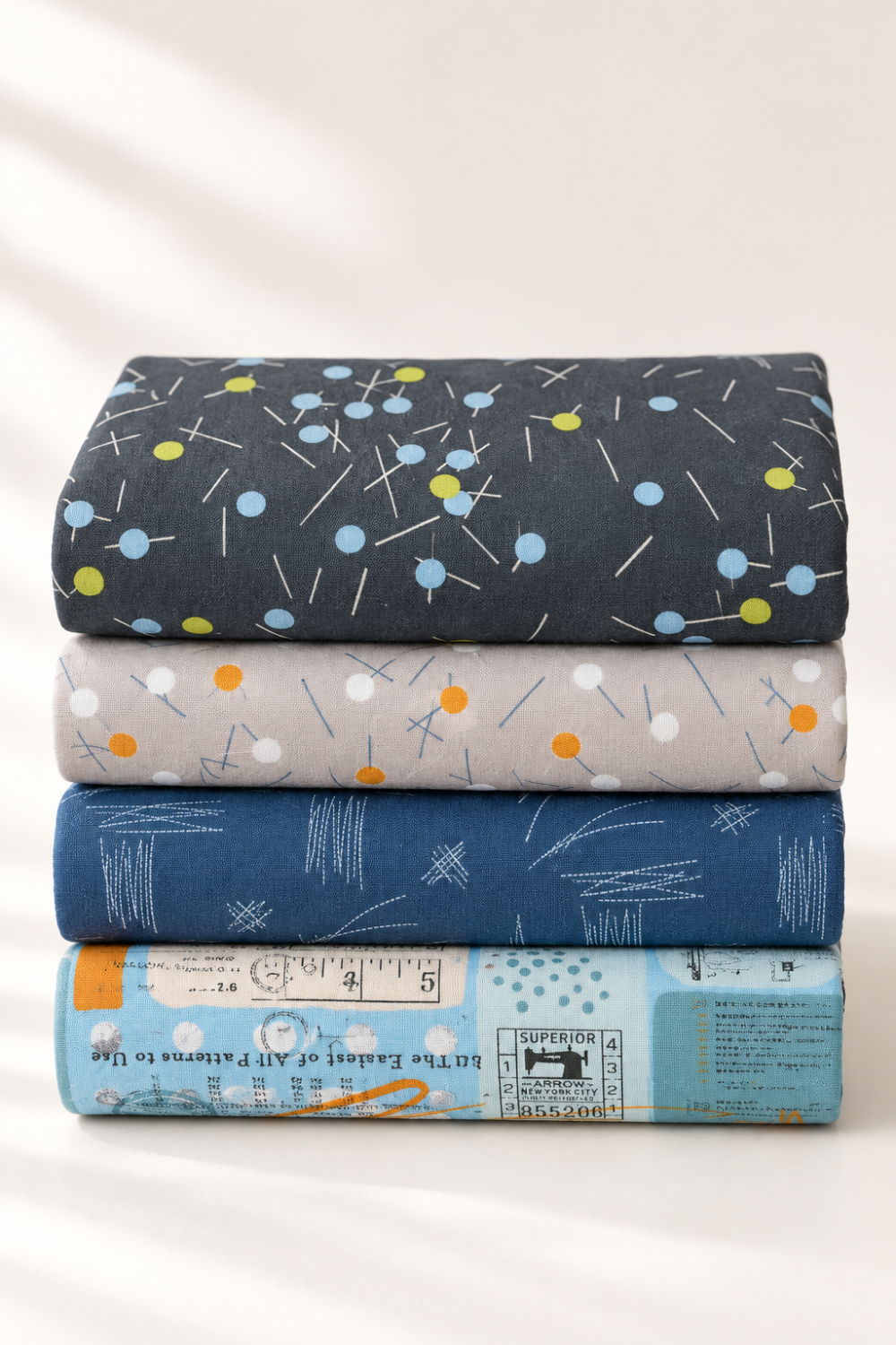 Vertical stack of coordinating modern quilting fabrics in charcoal, gray, navy, and pale blue, topped with Bluish Pins & Buttons Charcoal.