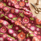 Superbloom Posy Party Zinnia fabric by Robin Pickens for Moda Fabrics, draped across a wooden sewing table beside scissors and a spool of thread.