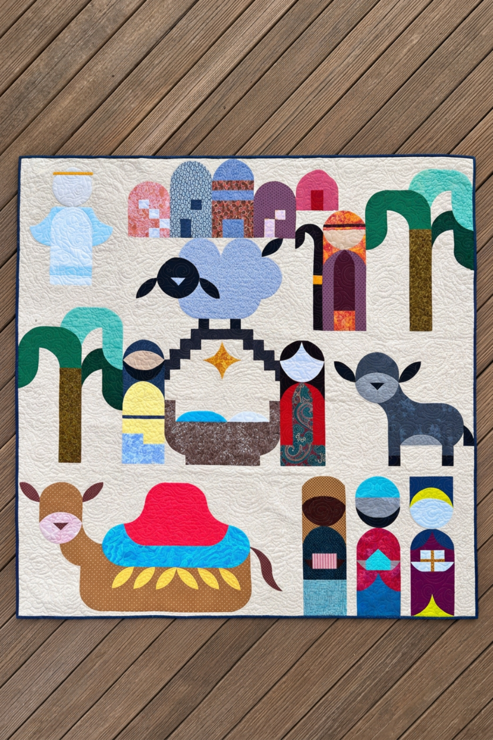 Starry Night handmade nativity quilt laid flat on wooden decking, featuring colorful figures, animals, palm trees, and a gold star.