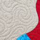 Close-up of Starry Night quilt showing spiral stitching on a light crosshatched background beside red and turquoise patchwork.