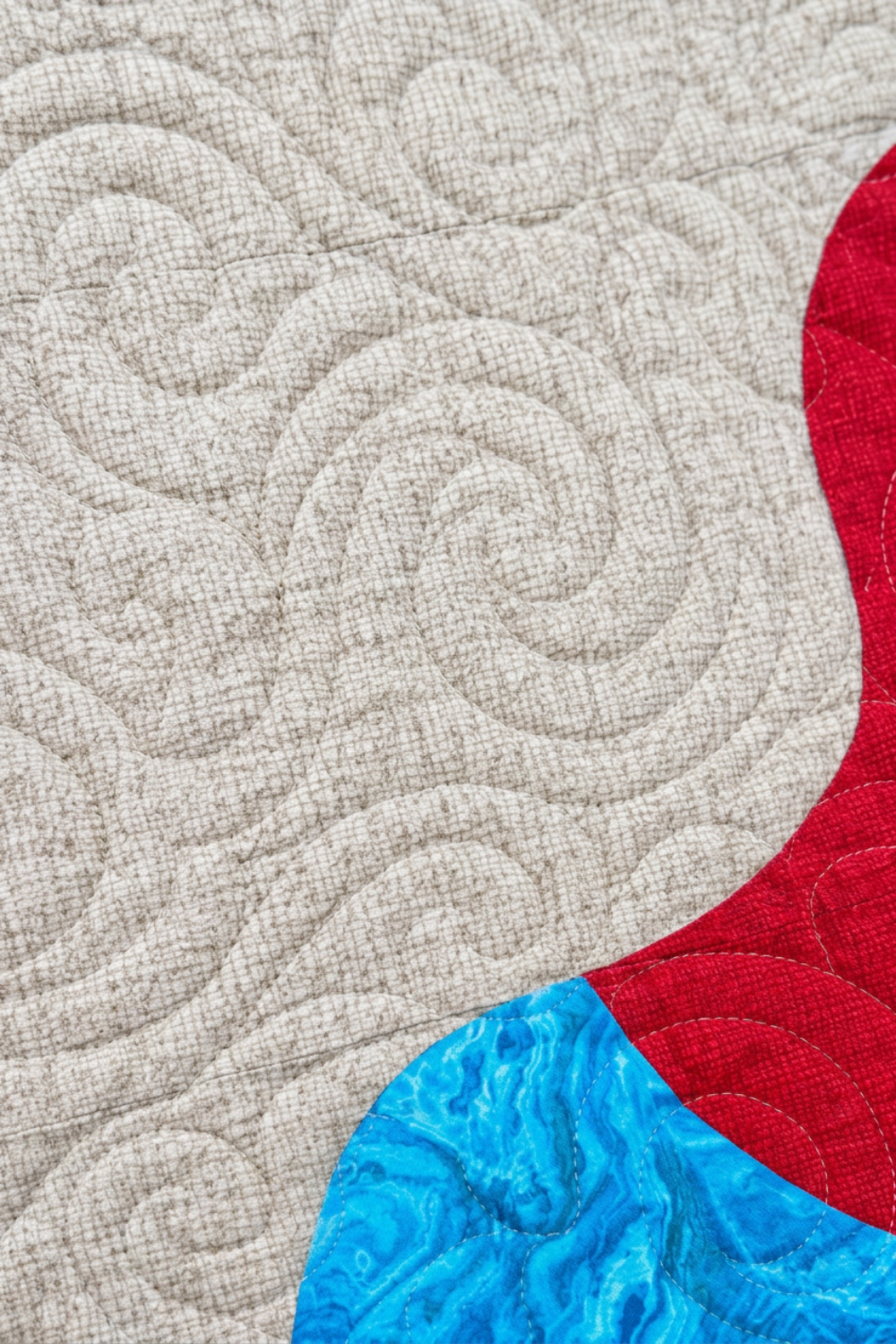 Close-up of Starry Night quilt showing spiral stitching on a light crosshatched background beside red and turquoise patchwork.