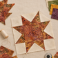 Unfinished traditional star quilt block featuring Windsong Floral Medallions Sienna batik, with cream background pieces, coordinating swatches, thread, clips, and a rotary cutter. Quilt block shown for inspiration. Coordinating fabrics and quilt patterns are available at IraRobi Quilts.