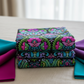 Vivid Brocade Jewel fabric by Jason Yenter for In The Beginning Fabrics folded in a stack on a light linen surface with coordinating jewel-toned magenta, teal, and purple fabrics – dramatic allover baroque brocade with magenta and purple damask florals and teal scrolling leaves on deep black, perfect for jewel-toned and floral quilt projects, 100% cotton, 3 yard cut