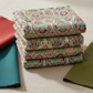 Vivid Brocade Spice fabric by Jason Yenter for In The Beginning Fabrics folded in a stack on a light linen surface with coordinating warm red, teal, and olive fabrics – dramatic allover baroque brocade with crimson and burgundy damask florals and teal scrolling leaves on warm cream, perfect for warm-toned floral and kaleidoscope quilt projects, 100% cotton, 3 yard cut