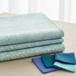 Vivid Mums Jewel Blue fabric by Jason Yenter for In The Beginning Fabrics folded in a stack on a light linen surface with coordinating periwinkle, teal, and aqua fabrics – dense allover chrysanthemum burst blender with tiny pointed petals in periwinkle blue, cobalt, teal, and aqua on very light pale blue and silver, perfect for jewel-toned and blue quilt projects, 100% cotton, 3 yard cut