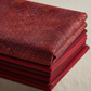 Vivid Mums Spice Red fabric by Jason Yenter for In The Beginning Fabrics folded in a stack on a light linen surface with coordinating deep red, burgundy, and plum fabrics – dense allover chrysanthemum burst blender with tiny pointed petals in deep crimson, red, coral-orange, and gold on dark burgundy, perfect for warm-toned and jewel-toned quilt projects, 100% cotton, 3 yard cut