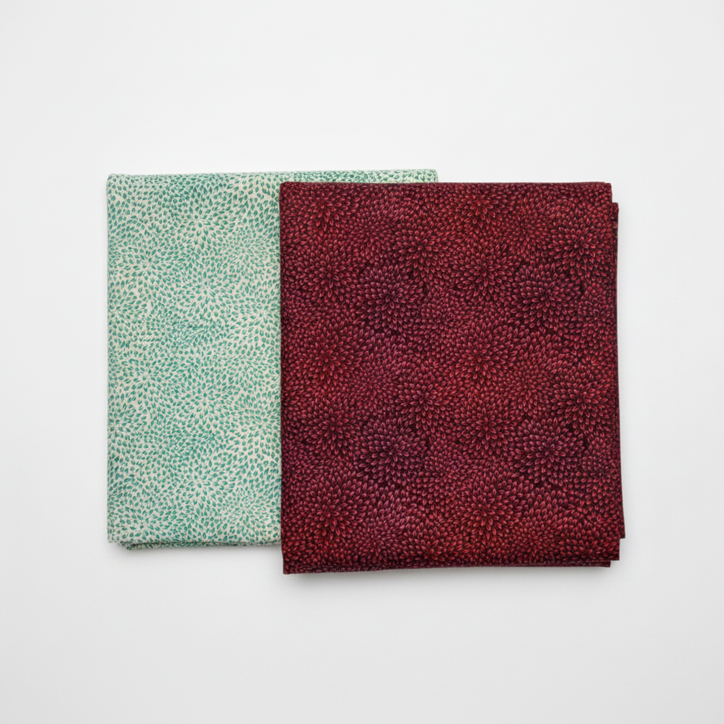 Vivid Mums Spice quilting cotton fabrics by Jason Yenter for In The Beginning Fabrics showing two colorways side by side – Vivid Mums Spice Teal with teal and emerald petals on light cream and silver-grey, and Vivid Mums Spice Red with deep crimson and red petals on dark near-black burgundy, same chrysanthemum burst pattern in two colorways, 100% cotton, 3 yard cuts