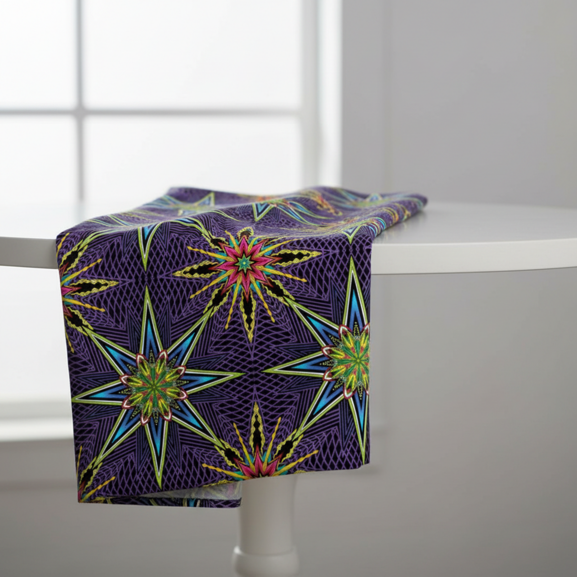 What If Radio Star Purple/Multi quilting cotton by Paula Nadelstern for Benartex — electric kaleidoscopic starbursts in sky blue, chartreuse, magenta, and yellow on deep violet and black — draped over a white table showing fabric hand and bold print scale, 100% cotton. Quilt blocks shown for inspiration. Coordinating fabrics and quilt patterns are available at IraRobi Quilts.