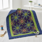 Modern medallion quilt featuring What If Radio Star Purple/Multi fussy-cut star blocks by Paula Nadelstern for Benartex — electric kaleidoscopic starbursts in sky blue, chartreuse, magenta, and yellow on deep violet and black — draped over a white linen sofa. Quilts shown for inspiration. Coordinating fabrics and quilt patterns are available at IraRobi Quilts.