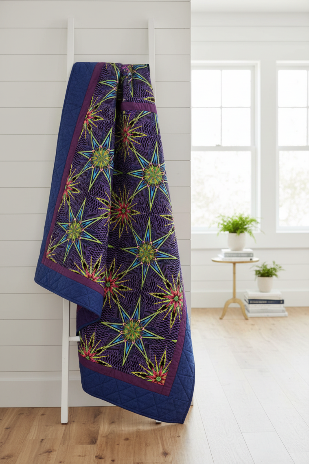 Modern medallion quilt with What If Radio Star Purple/Multi fussy-cut star blocks by Paula Nadelstern for Benartex and coordinating jewel-tone blender borders in plum and blueberry, draped over a white wooden ladder. Quilts shown for inspiration. Coordinating fabrics and quilt patterns are available at IraRobi Quilts.