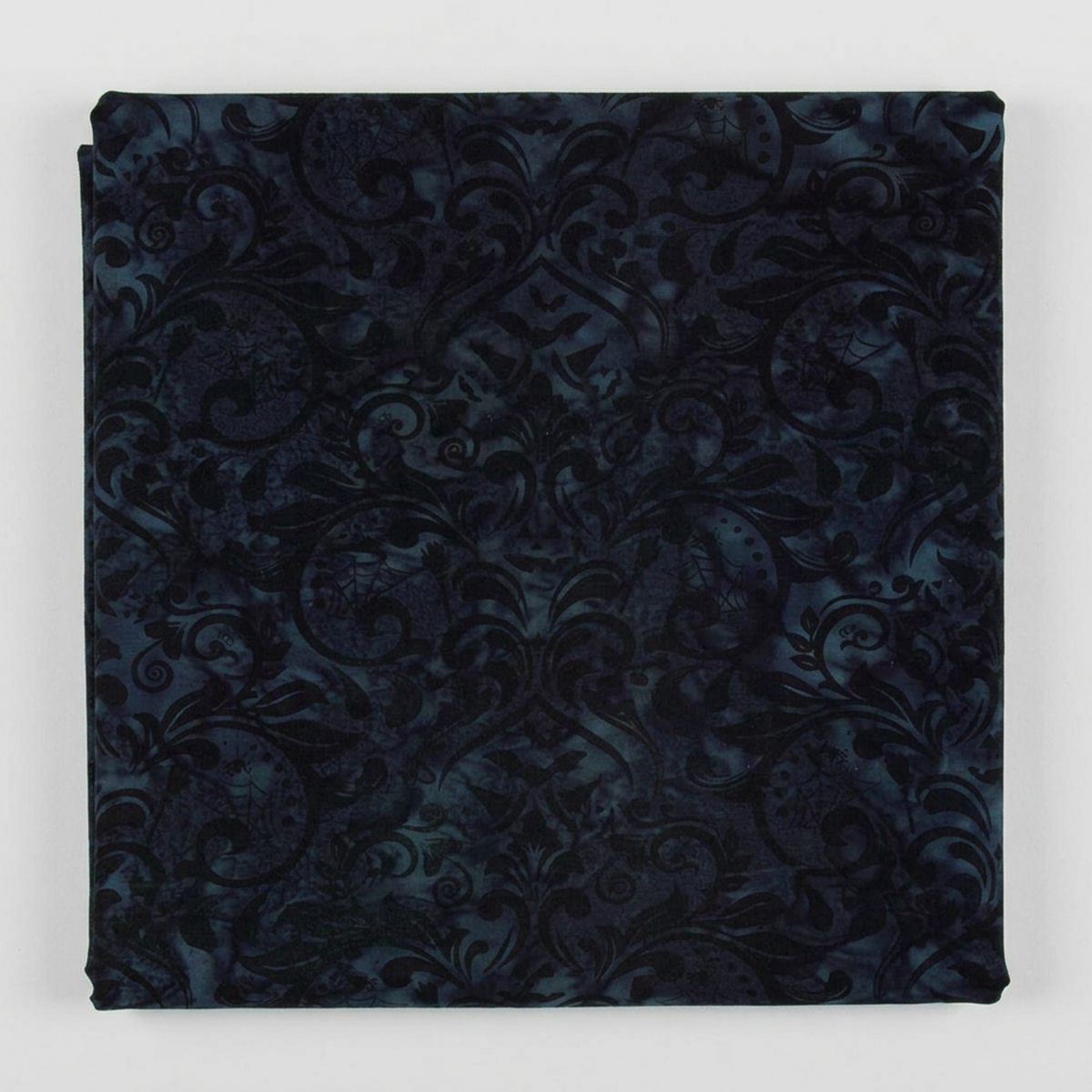 Folded Whispering Hollows Raven batik fabric by Riley Blake Designs, showing dark navy and black damask scrollwork against a light gray background.