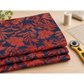 Folded Breezeway Red/Blue Textured Palms fabric on a sewing table beside a rotary cutter, ruler, thread, and pins.