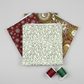 Winter Solstice II White Branches quilting cotton by Jason Yenter for In The Beginning Fabrics shown in a coordination stack with Red Snowflakes Metallic and Multi Celestial Metallic from the Winter Solstice II collection, with coordinating red, green, and cream thread bobbins. Quilt blocks shown for inspiration. Coordinating fabrics and quilt patterns are available at IraRobi Quilts.