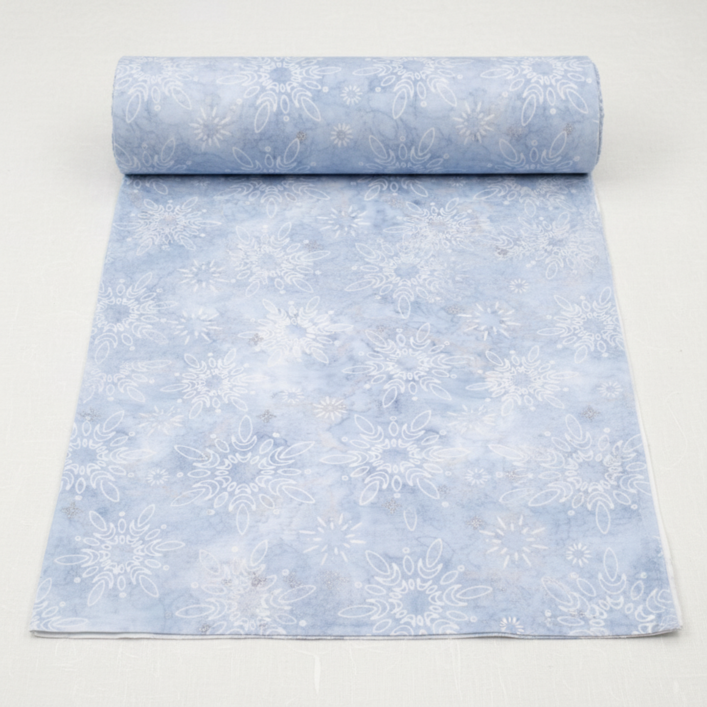 Winter Sparkle Glacier Artisan Batiks quilting cotton by Robert Kaufman Fabrics shown as a partially unrolled bolt with a cut yard of fabric displaying the full print repeat — soft powder blue tone-on-tone batik with white snowflake and daisy medallion motifs and silver metallic glitter accents.