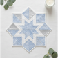 Winter snowflake star quilt block made with Winter Sparkle Glacier Artisan Batiks by Robert Kaufman Fabrics in soft powder blue with white snowflake motifs and silver metallic accents, paired with crisp white and pale silver companion fabrics. Quilt blocks shown for inspiration. Coordinating fabrics and quilt patterns are available at IraRobi Quilts.