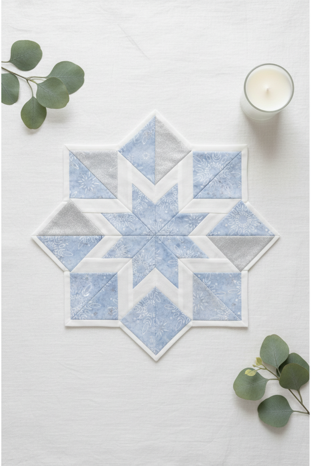 Winter snowflake star quilt block made with Winter Sparkle Glacier Artisan Batiks by Robert Kaufman Fabrics in soft powder blue with white snowflake motifs and silver metallic accents, paired with crisp white and pale silver companion fabrics. Quilt blocks shown for inspiration. Coordinating fabrics and quilt patterns are available at IraRobi Quilts.