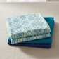 Wonders Of The Ocean Abstract fabric by Jason Yenter for In The Beginning Fabrics folded in a stack on a light linen surface with coordinating ocean blue and teal fabrics – allover ogee trellis lattice with Art Nouveau botanical medallions in turquoise, cobalt blue, and chartreuse green on white, perfect for coastal and ocean-themed quilt projects, 100% cotton, 3 yard cut