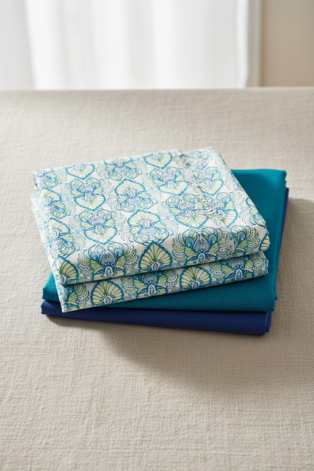 Wonders Of The Ocean Abstract fabric by Jason Yenter for In The Beginning Fabrics folded in a stack on a light linen surface with coordinating ocean blue and teal fabrics – allover ogee trellis lattice with Art Nouveau botanical medallions in turquoise, cobalt blue, and chartreuse green on white, perfect for coastal and ocean-themed quilt projects, 100% cotton, 3 yard cut