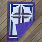 The Wondrous Cross wall quilt on wooden decking, with the lower-right corner folded back to reveal purple patterned backing and quilting stitches.
