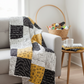 Patchwork quilt made with Writing on the Wall and Heat Wave FreeSpirit fabrics draped over grey sofa in cozy quilting room — black, white, and golden yellow word art prints