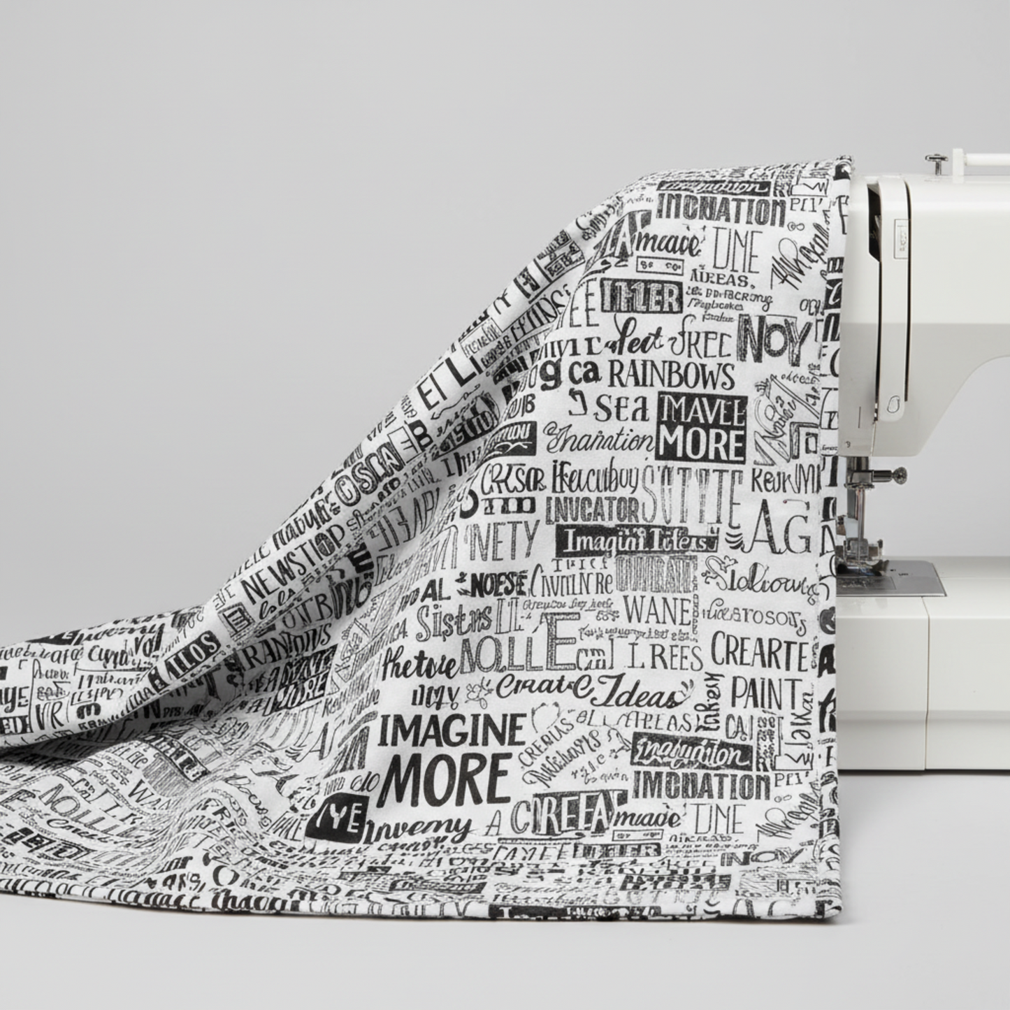 Writing on the Wall Word Collage White fabric draped over white sewing machine edge — black and white word collage quilting cotton by FreeSpirit Fabrics