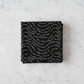 Writing on the Wall Script Black quilting cotton by FreeSpirit Fabrics -- three folded yards stacked on a white marble surface, bold black ground with free-flowing white script text in wave formations including Sea Sisters, Time and Tide, Touchstone, and discovery