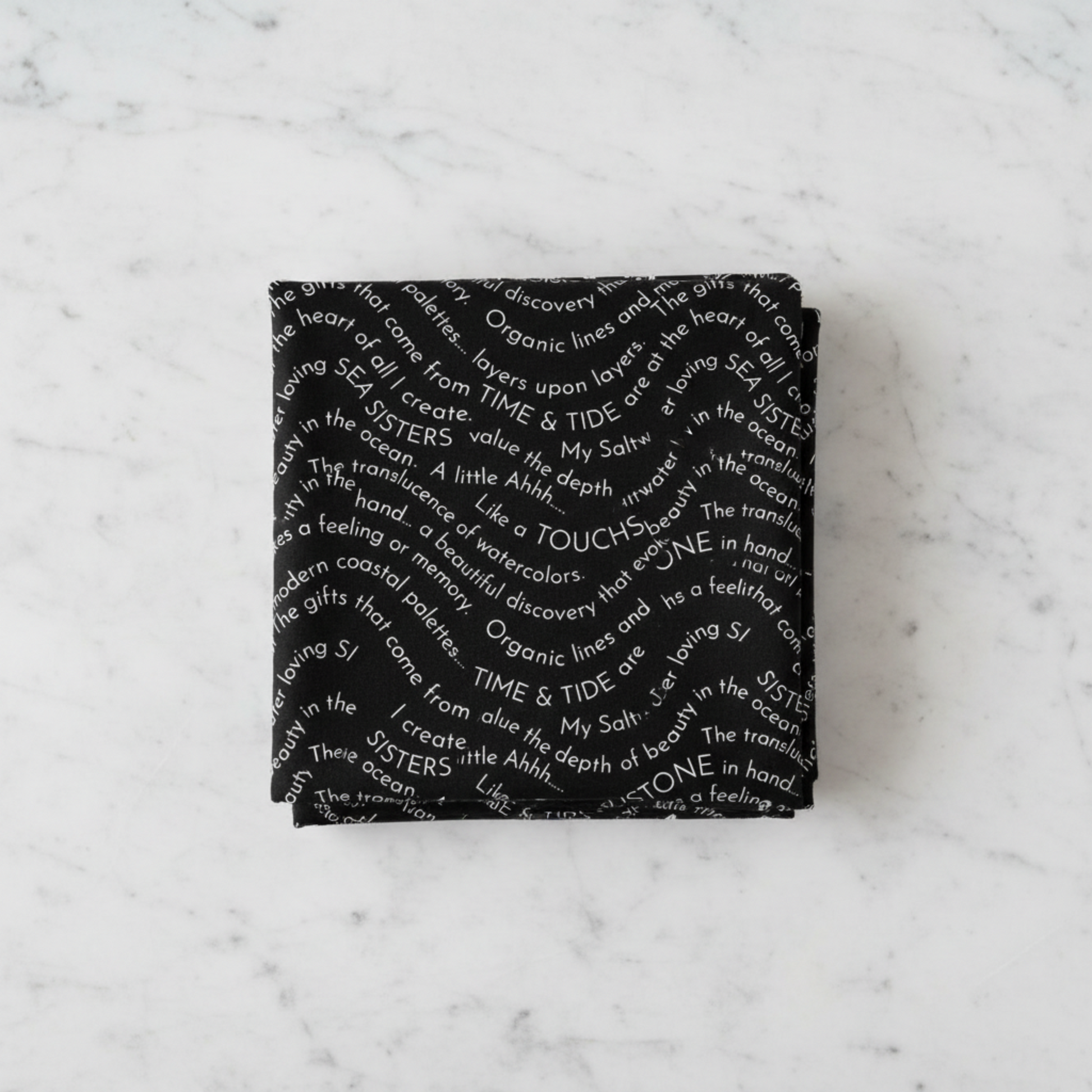 Writing on the Wall Script Black quilting cotton by FreeSpirit Fabrics -- three folded yards stacked on a white marble surface, bold black ground with free-flowing white script text in wave formations including Sea Sisters, Time and Tide, Touchstone, and discovery