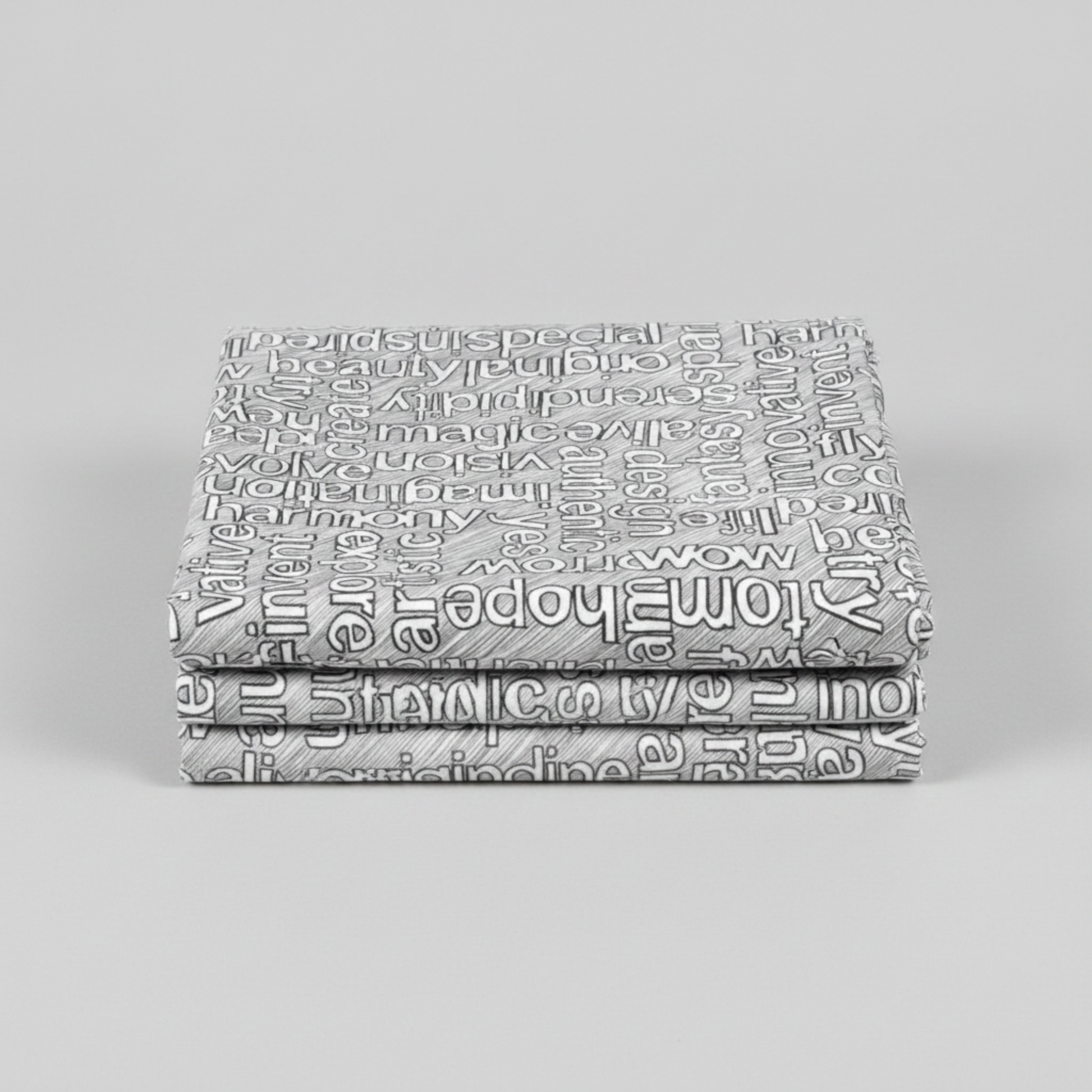 Writing on the Wall Well Worded White quilting cotton by FreeSpirit Fabrics -- three folded yards stacked on a grey surface, grey and white ground with white outlined words in varying sizes and directions including special, beauty, serendipity, magic, imagination, harmony, wow, and tomorrow