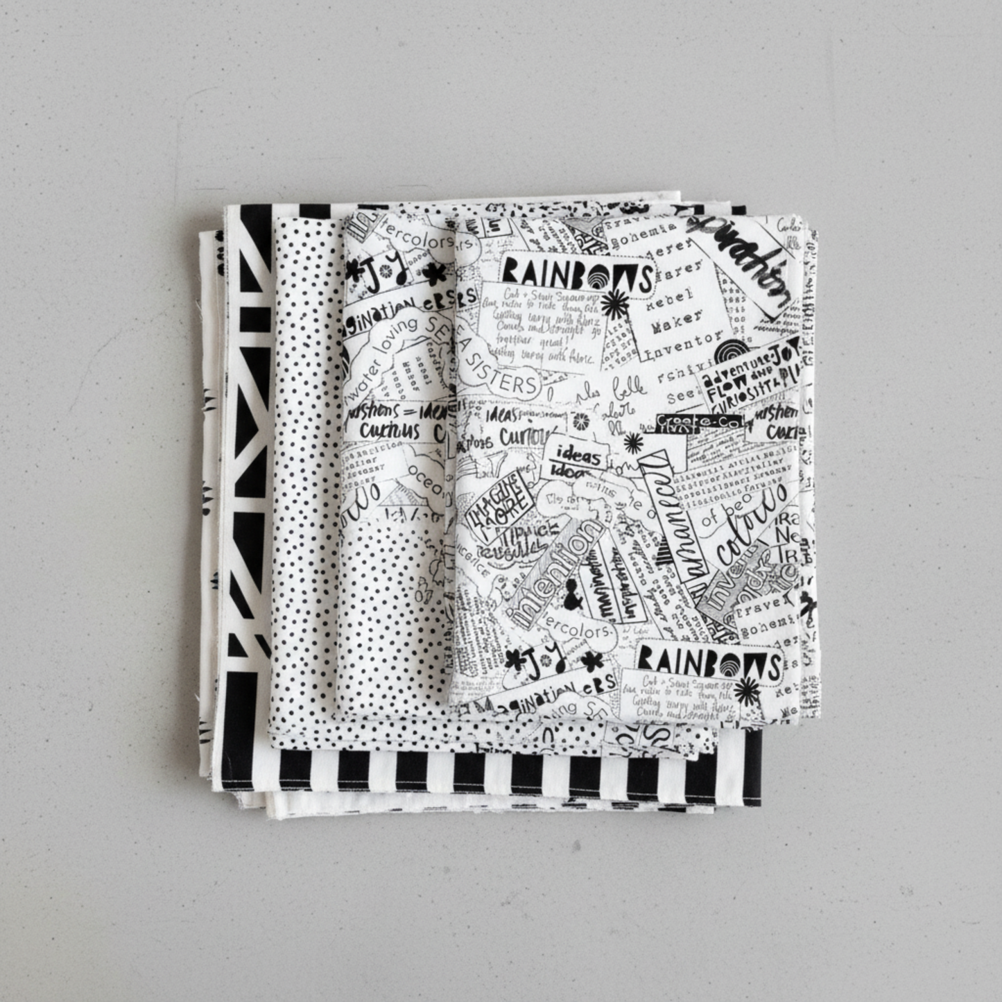 Writing on the Wall Word Collage White quilting cotton by FreeSpirit Fabrics — coordination stack of four modern black and white fabrics fanned on light grey background, including bold word collage, geometric, dot, and stripe prints