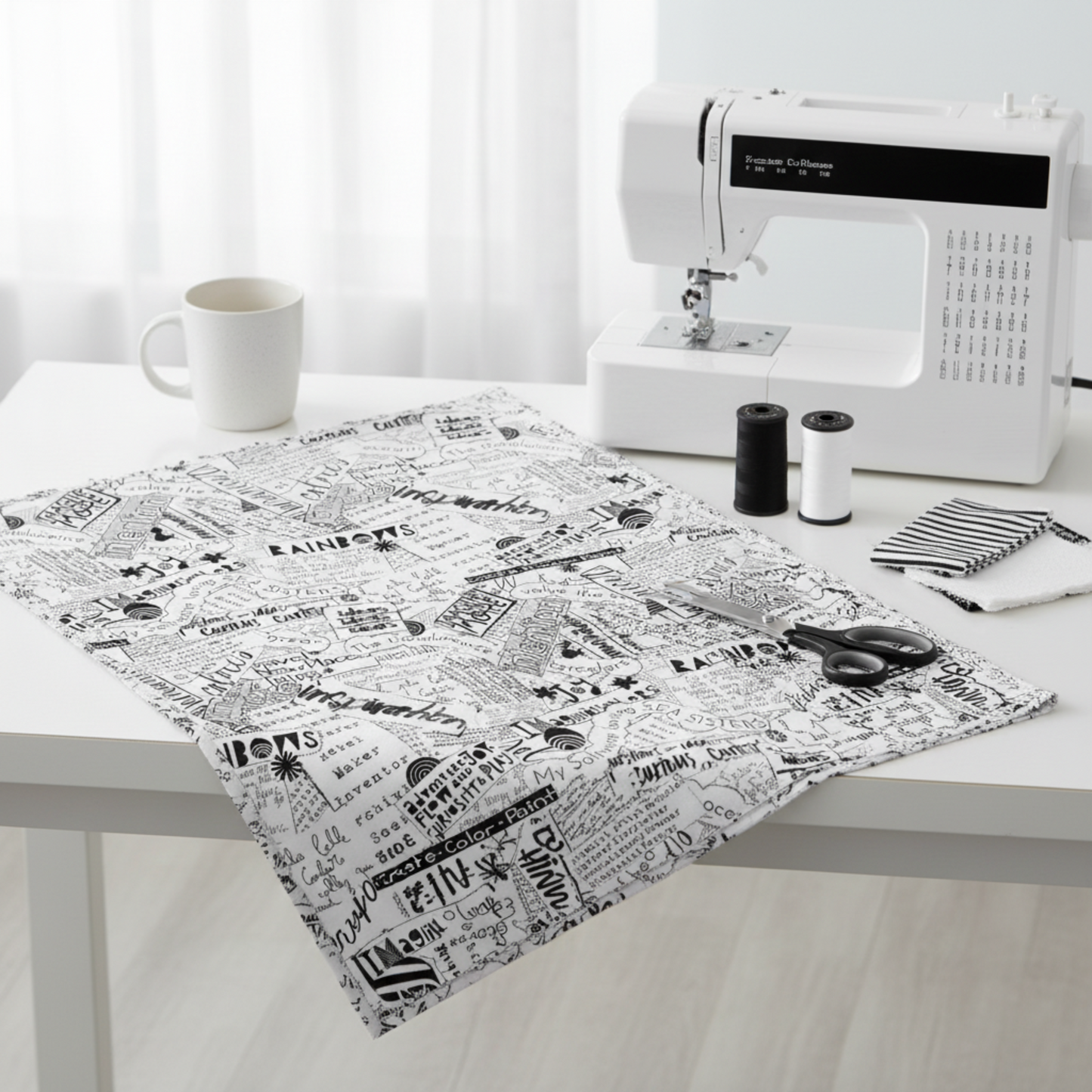 Writing on the Wall Word Collage White quilting cotton by FreeSpirit Fabrics — styled modern sewing room flat lay with bold black and white word collage fabric alongside sleek sewing machine, black and white thread spools, scissors, and coordinating black and white fabric swatches